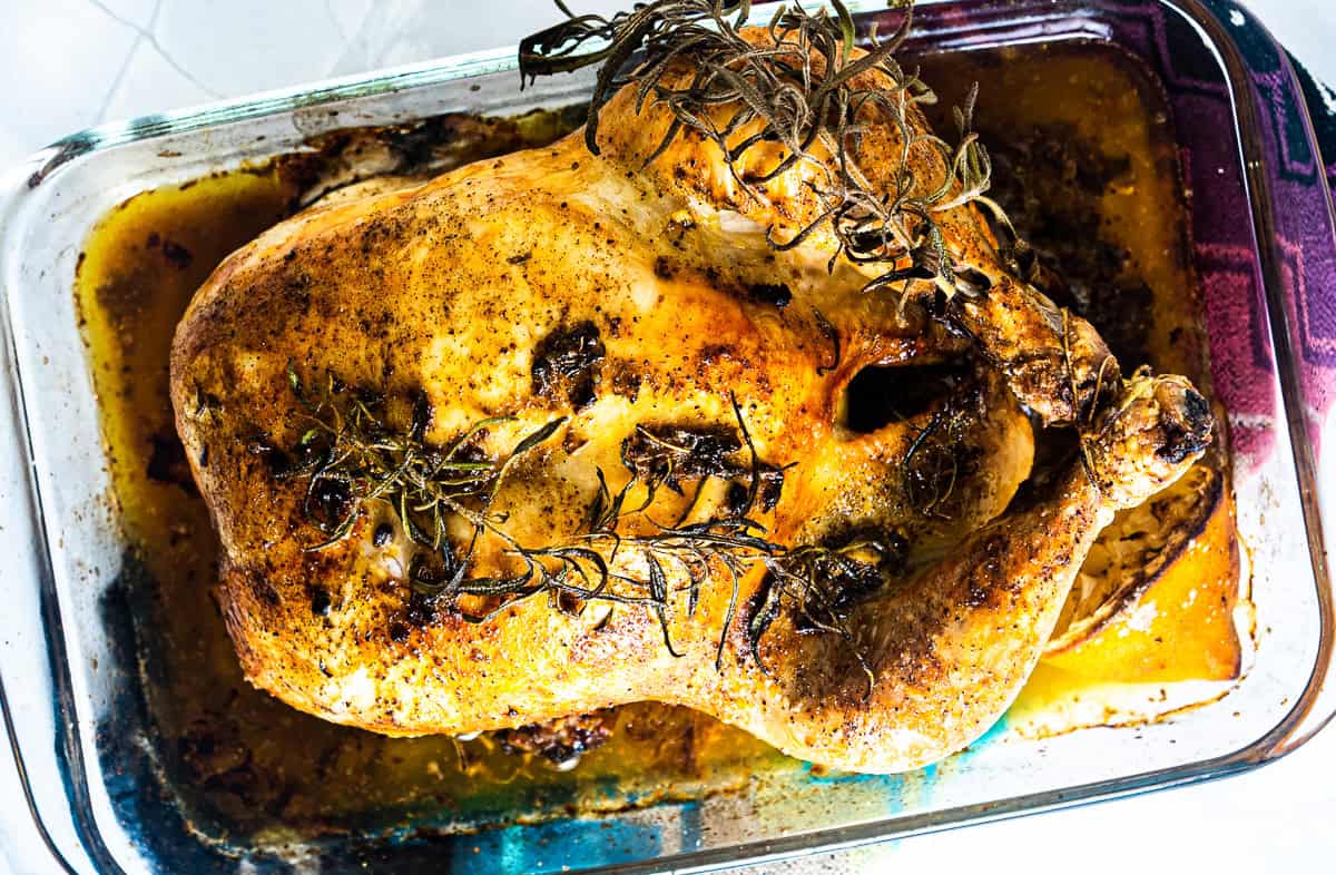 En hel kylling med urter ligger i en glassform, omgitt av smeltet kryddersmør.