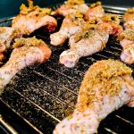 Rå, krydret kyllinglår i ovn anrettet på en metallrist over et stekebrett, klar til steking.