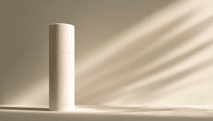 En høy, deodorant-beholder med hjemmelaget deodorant står oppreist mot en beige vegg, mens sollyset kaster diagonale skygger over scenen.