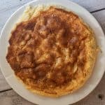 En gyllenbrun eplekake ligger på en hvit tallerken på et rustikt underlag av tre.