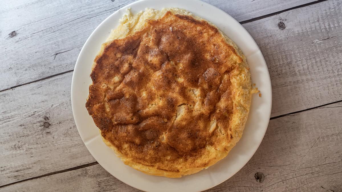 En gyllenbrun eplekake ligger på en hvit tallerken på et rustikt underlag av tre.