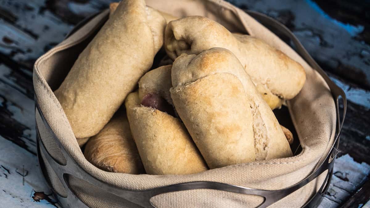 I en kurv ligger det flere gyllenbrune ost- og skinkehorn, noen med små sprekker i overflaten.