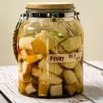 En glasskrukke med trelokk inneholder oppkuttede fermenterte fruktbiter merket "FRUKT 22,1", som står på en lys treflate.