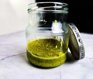 En åpen glasskrukke med grønt pistasj-smør med lokket hvilende på siden, plassert på en hvit flate.