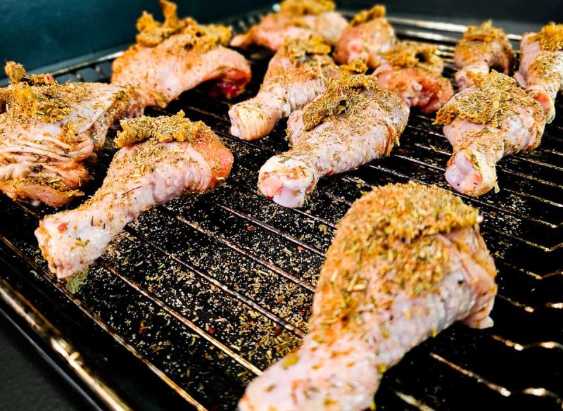 Rå, krydret kyllinglår i ovn anrettet på en metallrist over et stekebrett, klar til steking.