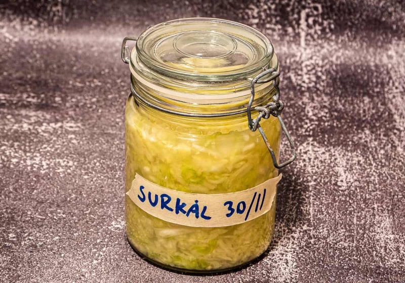 På en strukturert flate står et glass med surkål og en håndskrevet etikett med teksten "SURKÅL 30/11".